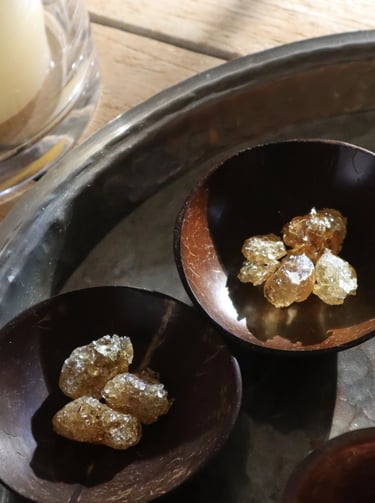 Golden frankincense resin pieces in small dark wooden bowls on a rustic metal tray.