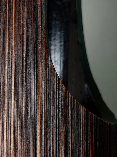 Close-up of polished dark wood grain with a smooth curved cutout revealing a glossy black interior.