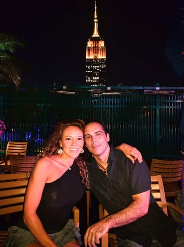 Travel bloggers on New York City rooftop at night with illuminated Empire State Building in backgrou