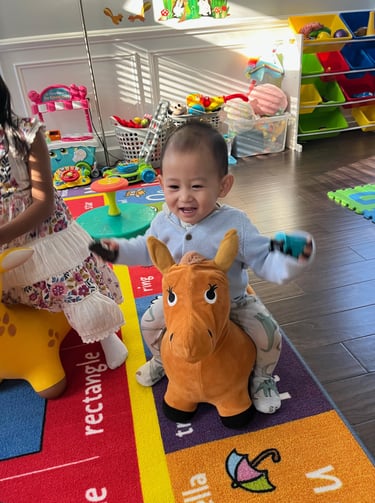 Photo of young child laughing while playing on a toy horse.