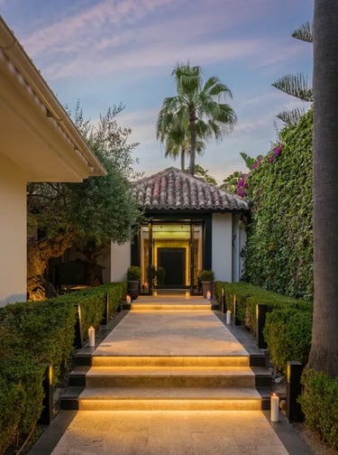 Illuminated entrance pathway framed by lush greenery and palm trees at Villa El Olivo, Marbella