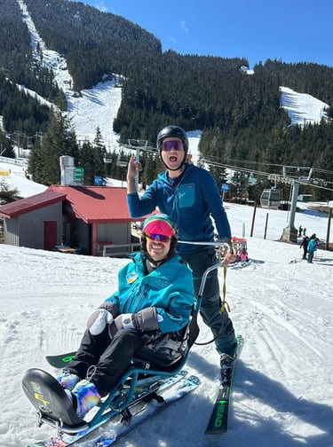 Sean in his sit ski with instructor Adria both wearing instructor jackets with big smiles on