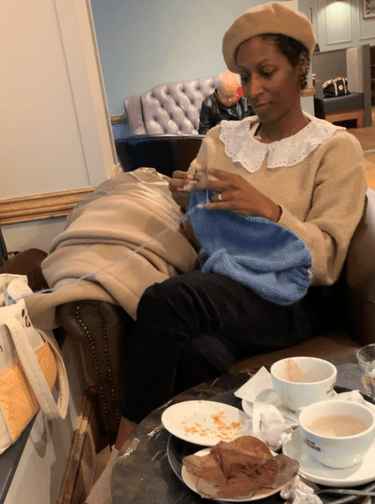 a woman sitting on a couch with a cup of tea and she is knitting