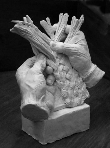 A detailed clay sculpture of two hands skillfully weaving a basket with long fibers on a square base.