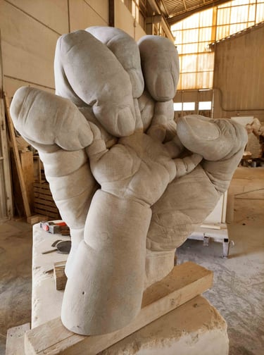 Giant stone sculpture of a baby's hand nestled inside a large adult hand in an artist's workshop.