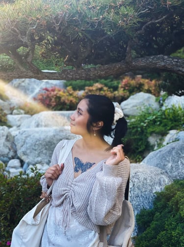 Me in a Japanese garden, holding ponytail looking left. Shows chest tattoo of a distorted butterfly.