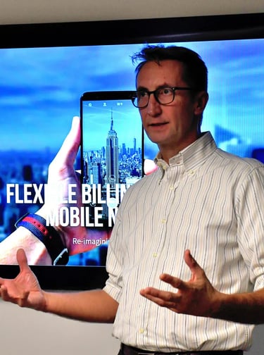 a man standing in front of an audience with a tv in the background