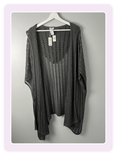Charcoal gray open front crochet knit cardigan wrap hanging on a white hanger against a gray wall.
