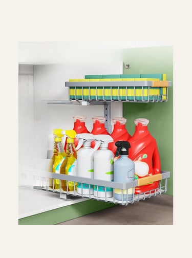 Two-tier pull-out metal cabinet organizer filled with cleaning spray bottles, detergent, and sponges.