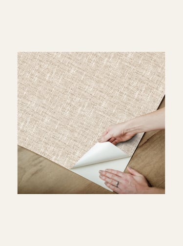 Hands applying beige grasscloth peel and stick textured wallpaper to a surface, showcasing easy DIY home decor updates.