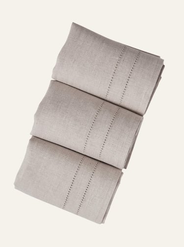 Three folded beige linen napkins with elegant hemstitch detailing for a neutral table setting.