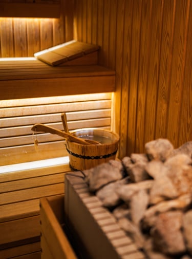 Traditional wooden sauna interior featuring hot stones, a water bucket, and a wooden ladle.