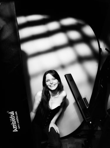 A smiling woman poses for a black and white studio portrait with dramatic gobo lighting patterns.