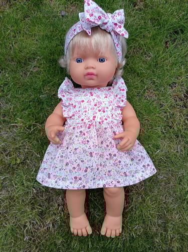 Miniland doll dressed in a pink floral dress with ruffles