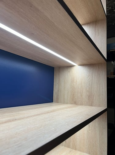 Modern light wood floating shelves featuring integrated LED strip lighting and a navy blue accent wall.