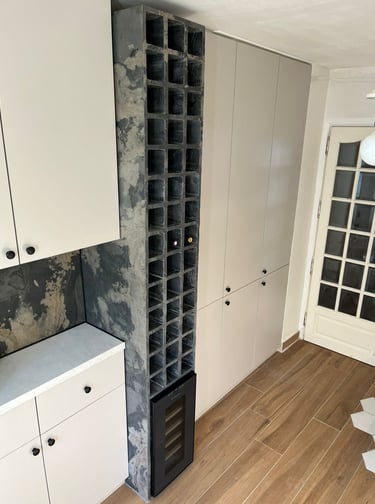 Modern kitchen with white cabinets, wood floors, and a floor-to-ceiling concrete wine rack.