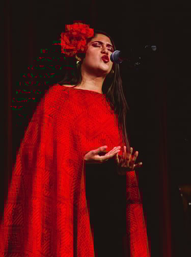 Female singer performing on stage in a red embroidered shawl and floral hair accessory.