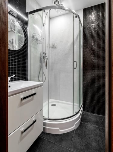 Bathroom with corner glass shower enclosure and black mosaic tiled walls