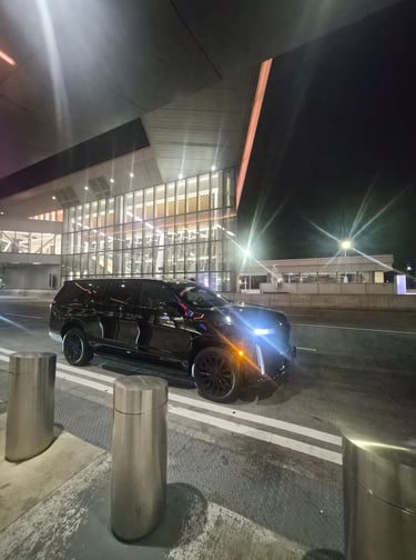 Black luxury Cadillac Escalade SUV parked at night outside a modern glass airport terminal.