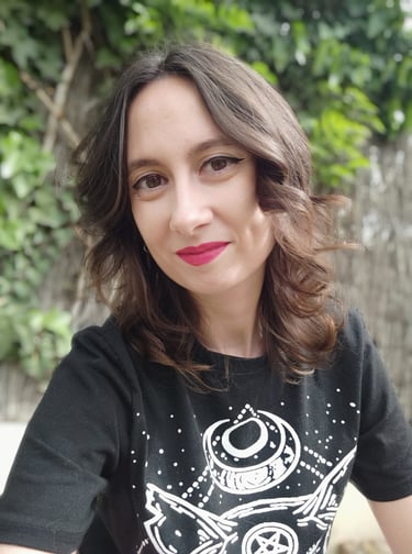 Foto de Reah, la creadora de ADOM. Una mujer castaña vestida de negro sobre un fondo verde de jardín