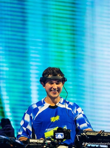 john summit in a blue shirt and headphones on a dj booth