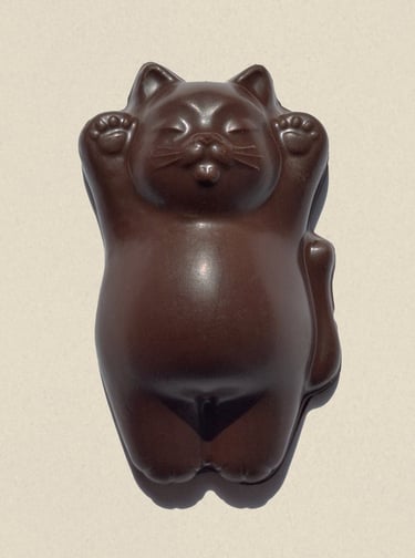 A brown chocolate maneki-neko lucky cat figurine with raised paws on a beige background.