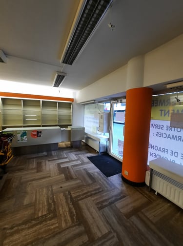 Commerce avant transformation avec un espace vide, une grande vitrine et de grands poteaux orange