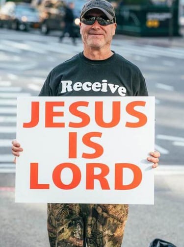Man holding a sign that reads ‘Jesus Is Lord,’ expressing public faith.