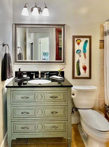 Bathroom with vintage emerald vanity, black granite countertop, and beveled glass mirror.