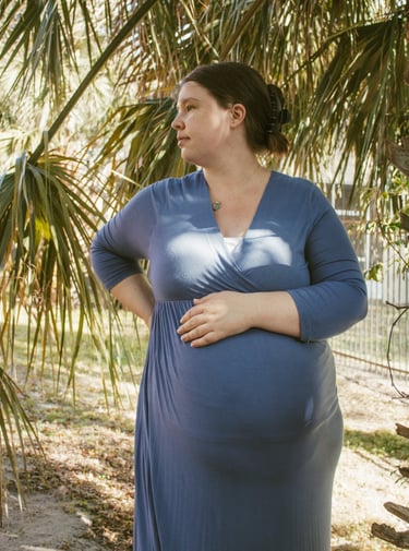 a pregnant woman in a blue dress standing in front of a palm tree