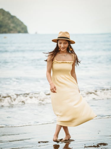 portrait of a woman in a yellow dress and hat walking on the beach in jaco