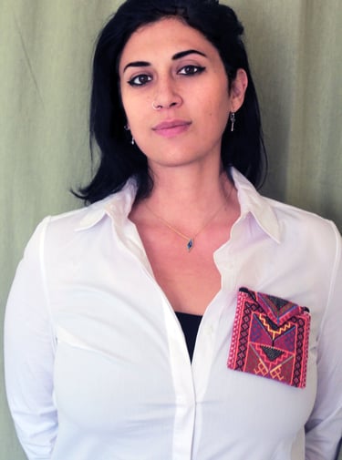 A woman wearing a white button-down shirt featuring a colorful embroidered textile pocket.