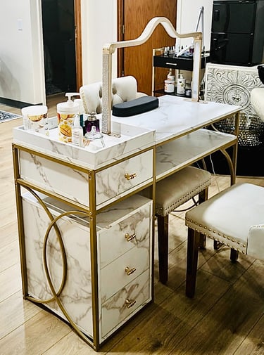 Elegant marble and gold manicure table with desk lamp, storage drawers, and matching white nail technician chairs.
