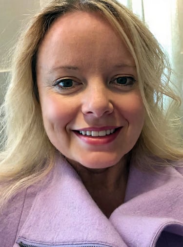 A smiling blonde woman wearing a purple coat, showcasing a professional headshot for profile use.