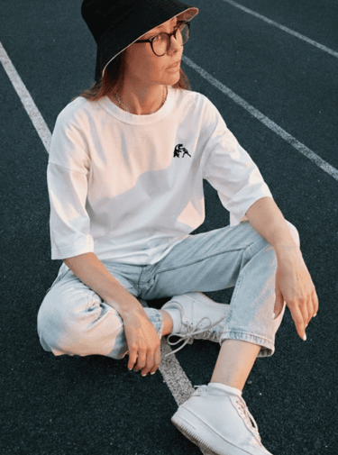 Mujer con camiseta blanca y sombrero tipo pescador, usando tenis, en una pista de atletismo.