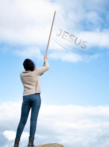 a woman holding a jesus flag on a rock