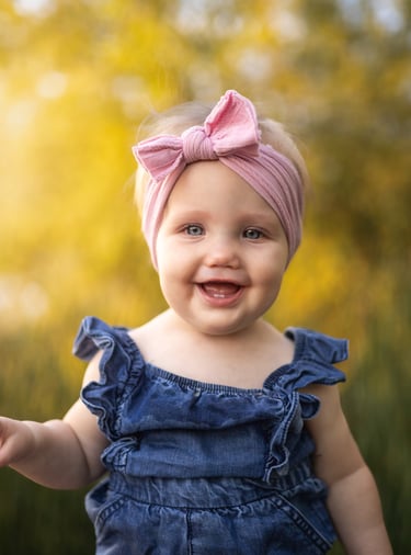 Smiling baby wearing a pink bow during an outdoor portrait session.