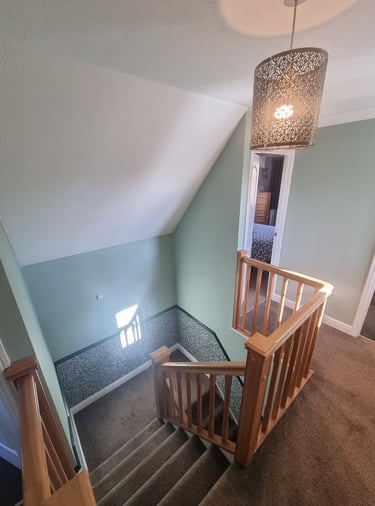 A carpeted staircase in a house, with surrounding half painted-green walls, and half wallpapered.