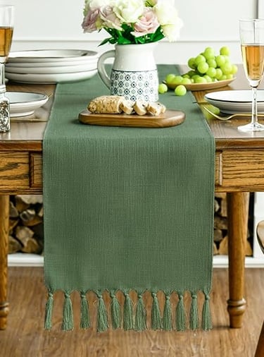 Green boho table runner with textured fringe detail, displayed on a natural wooden dining table.