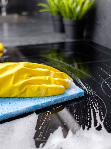 a person cleaning wearing yellow rubber gloves cleaning a stove top