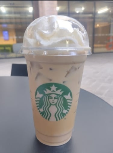 Iced caramel macchiato with whipped cream in a Starbucks takeaway cup on a black table, perfect summer coffee beverage