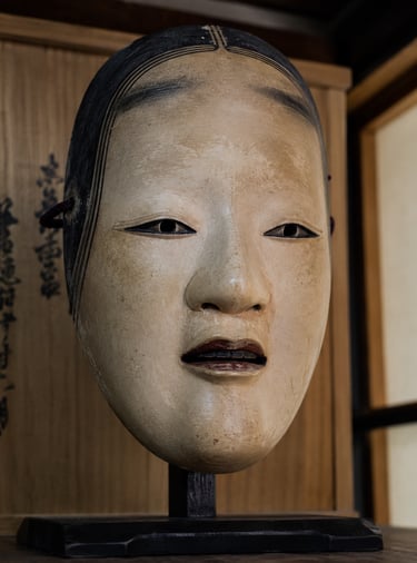 Antique carved wooden Japanese Noh mask of a woman displayed on a stand with a calligraphy box background.