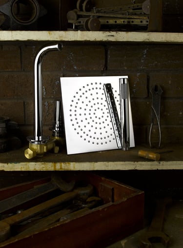 square chrome rain shower head and tap on a shelf in an old workshop