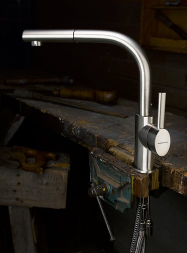 brushed stainless steel kitchen mixer tap held in the vice of an old wooden work bench