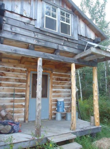 the porch of a rustic wood cabin, with a cooler for water resting on a makeshift shelf