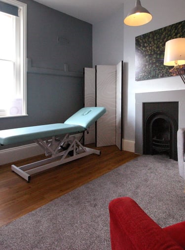 Modern private treatment room featuring a professional massage table, fireplace, and comfortable therapy chairs.