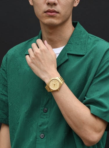 Young man wearing a green printed short-sleeve shirt and a luxury gold watch on a dark background.
