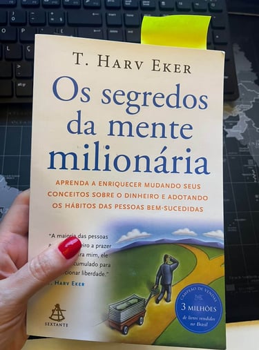 Portuguese edition of Secrets of the Millionaire Mind by T. Harv Eker held over a laptop.