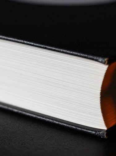 High-contrast macro photograph of a physical book spine, deep shadows, crisp white paper edges visible, dramatic orange accent light from the side.