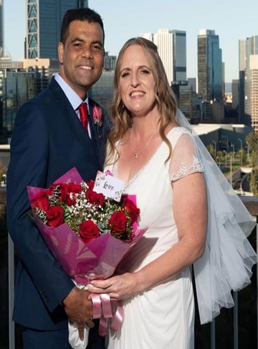 Salome and Richard on their wedding day, standing together with a bouquet and city skyline behind th